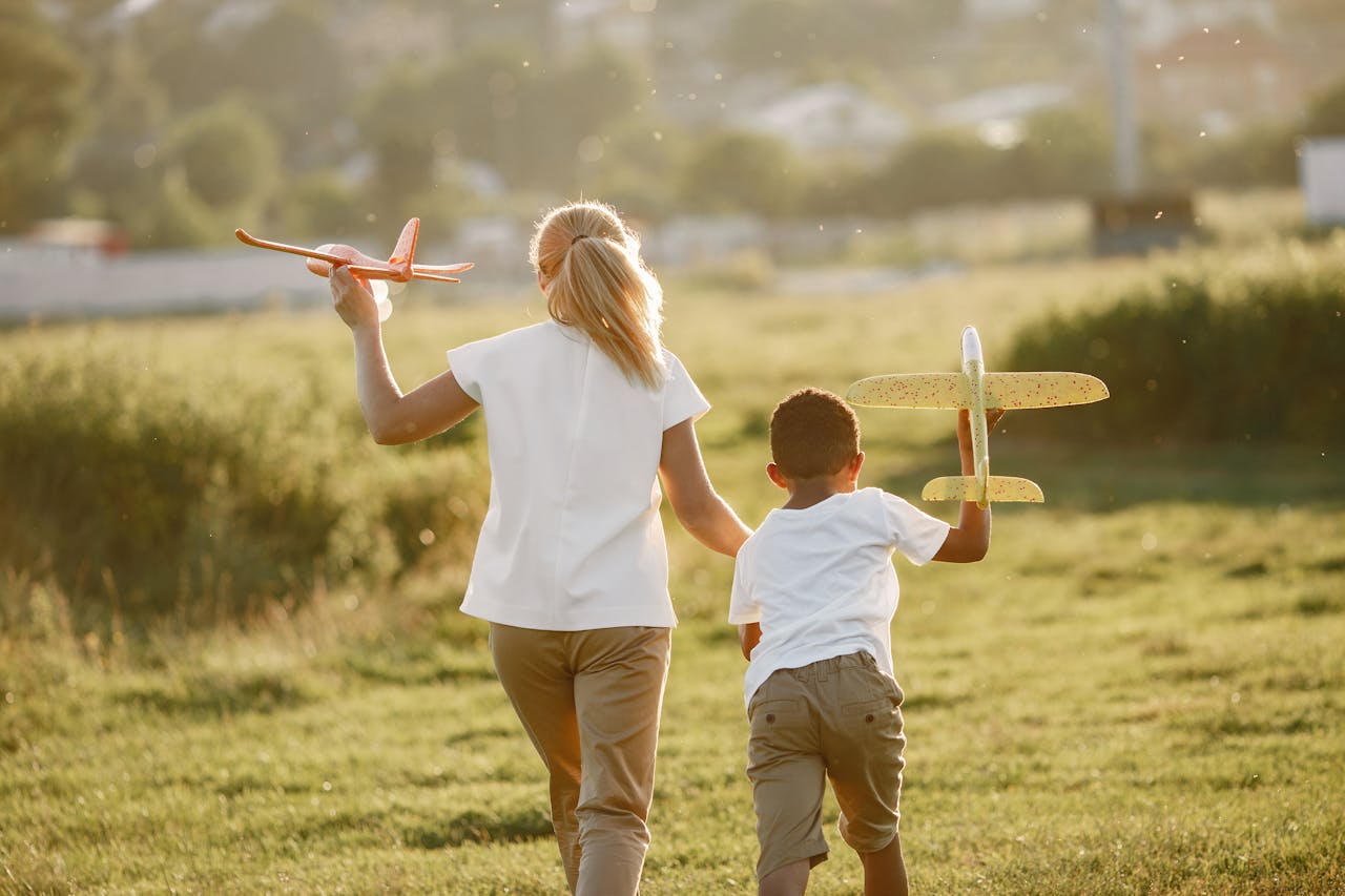 Two children enjoy playing with toy planes in an open green field during the day.